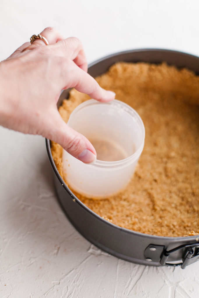 pressing down a graham cracker crust in a springform pan 