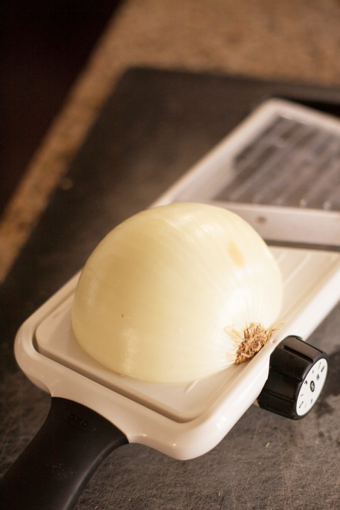 Half a white onion waiting to be sliced on a mandoline.