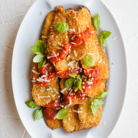 Fried Zucchini Planks on white oval plate topped with marinara sauce and basil