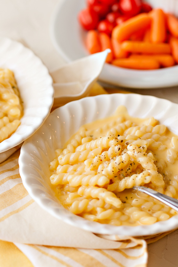 Homemade macaroni and cheese in a bowl with carrots and tomatoes in the backgroun