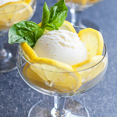 Fresh lemon ice cream in a glass serving cup with lemon slices and basil
